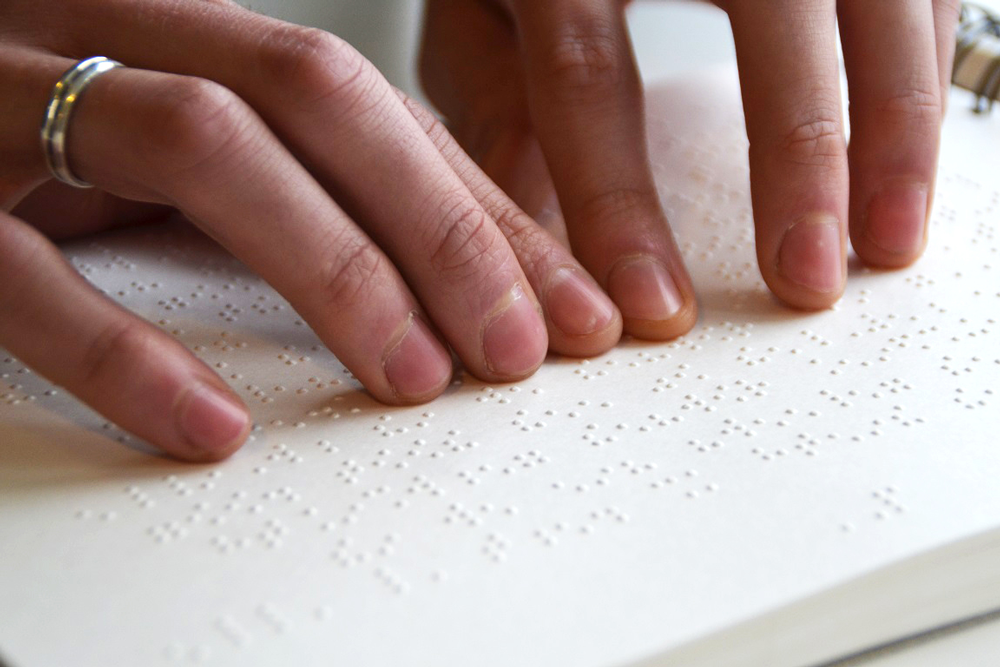 twee handen voelen een pagina met braille