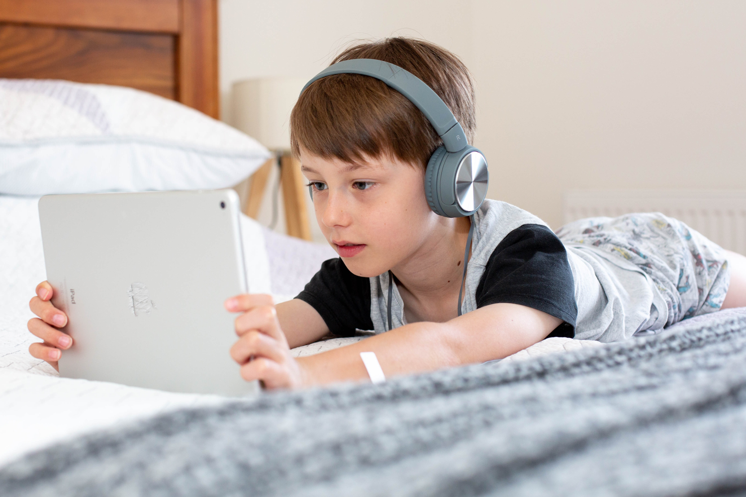 jongen, liggend op bed, leest met koptelefoon en ipad in de handen