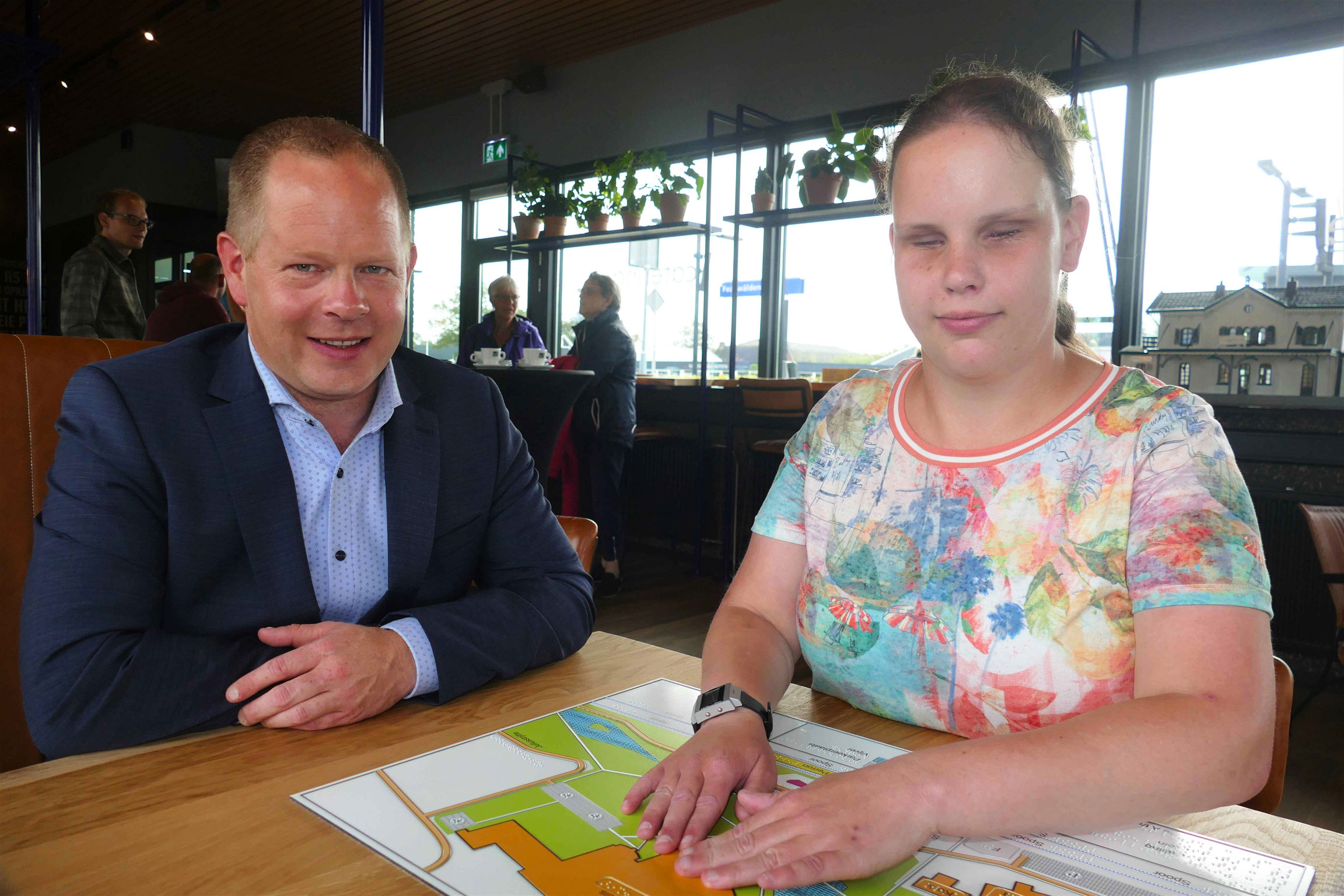 Wethouder Kees Wielstra en Nynke Sipma zitten aan een tafel en Nynke voelt een tactiele plattegrond