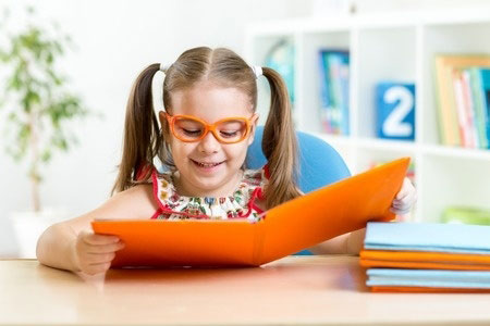 Meisje met twee staartjes en bril leest in een groot boek