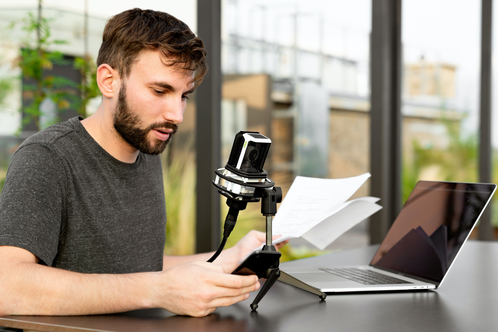 Man met baard leest een document voor in microfoon. Laptop op tafel.