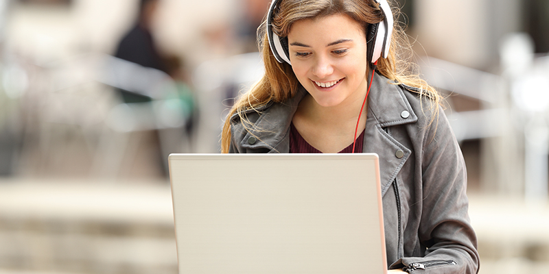 tiener meisje lachend met koptelefoon achter een laptop