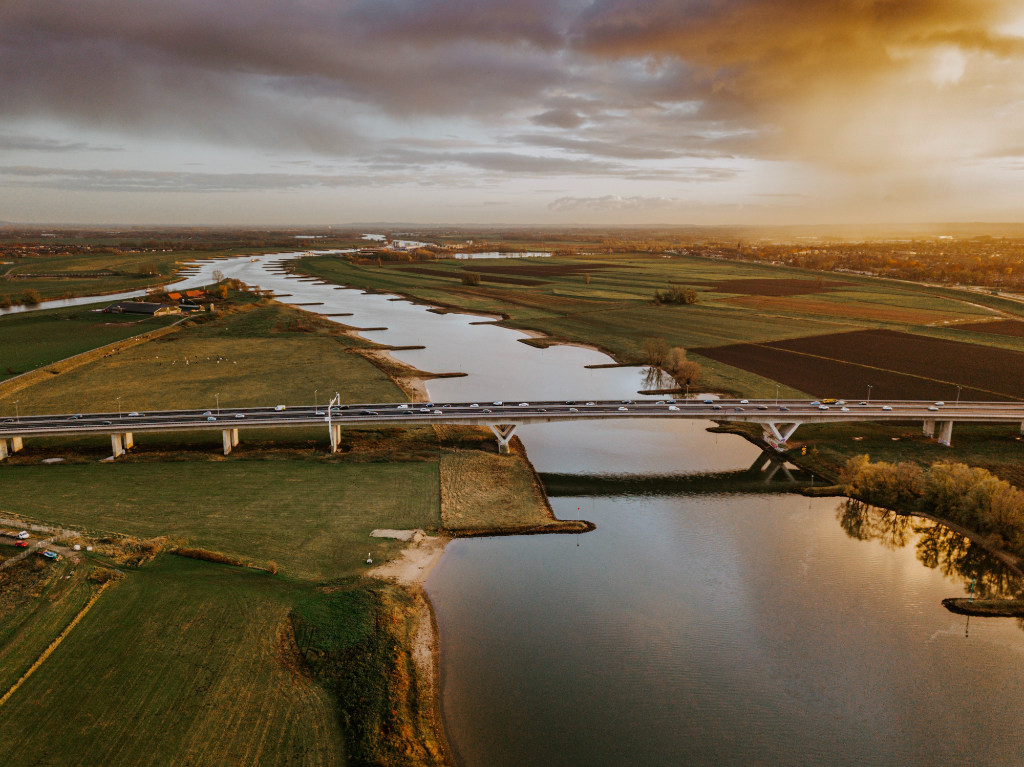 Nederlands landschapsfoto van een polder; rivier met daarover een brug waarover auto's rijden