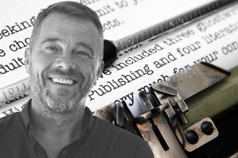 glimlachende man van middelbare leeftijd met baard met op de achtergrond een getypt vel papier in oude typemachine