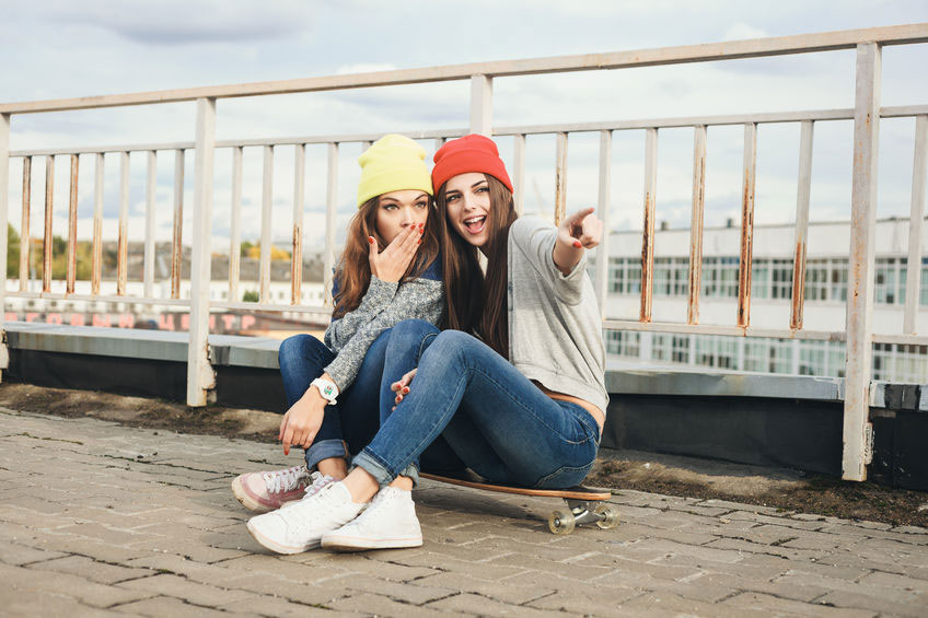 twee tienermeiden met mutsjes zitten op een skateboard