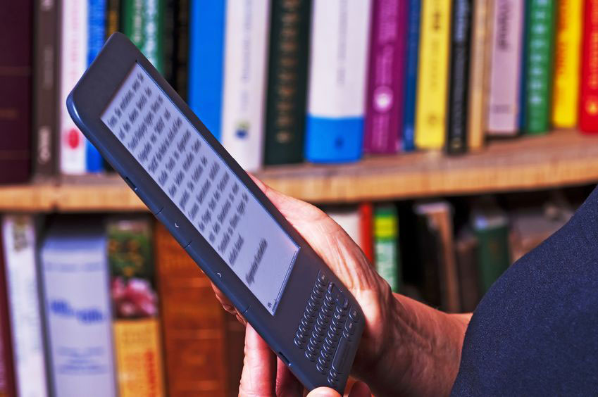 Een persoon houdt een e-reader vast; op de achtergrond een volle boekenkast.