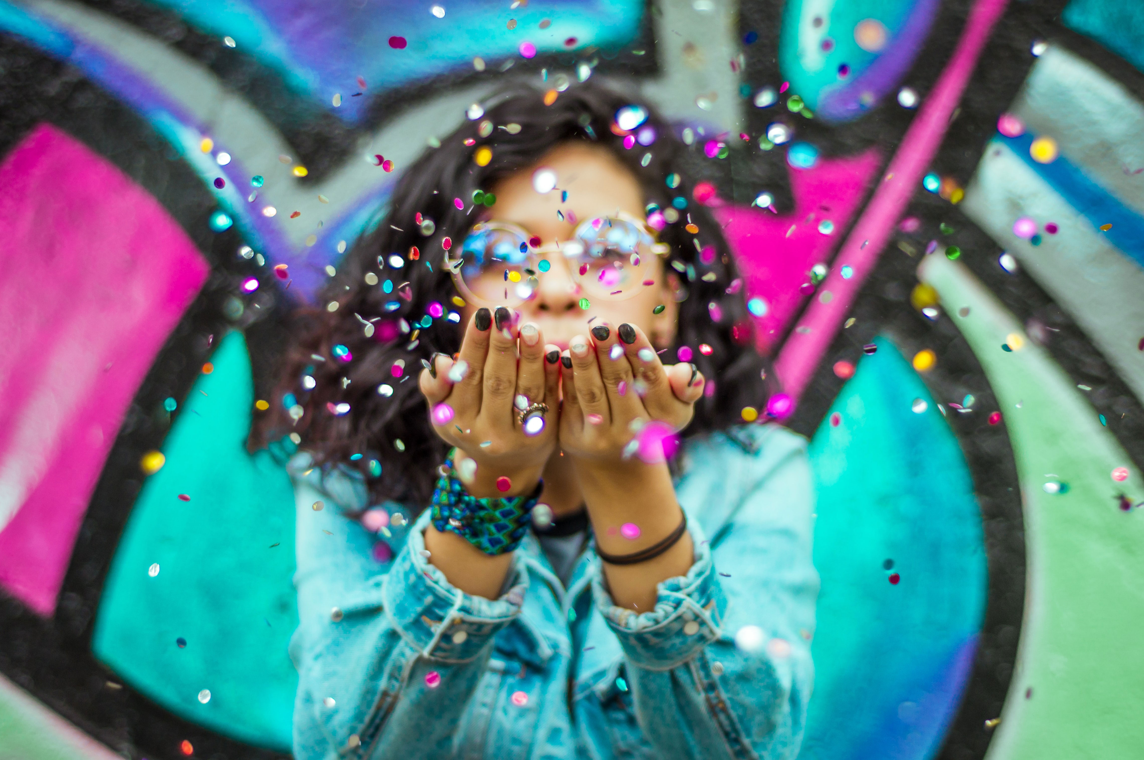 Jonge dame blaast confetti naar de camera. Grafitti achtergrond.