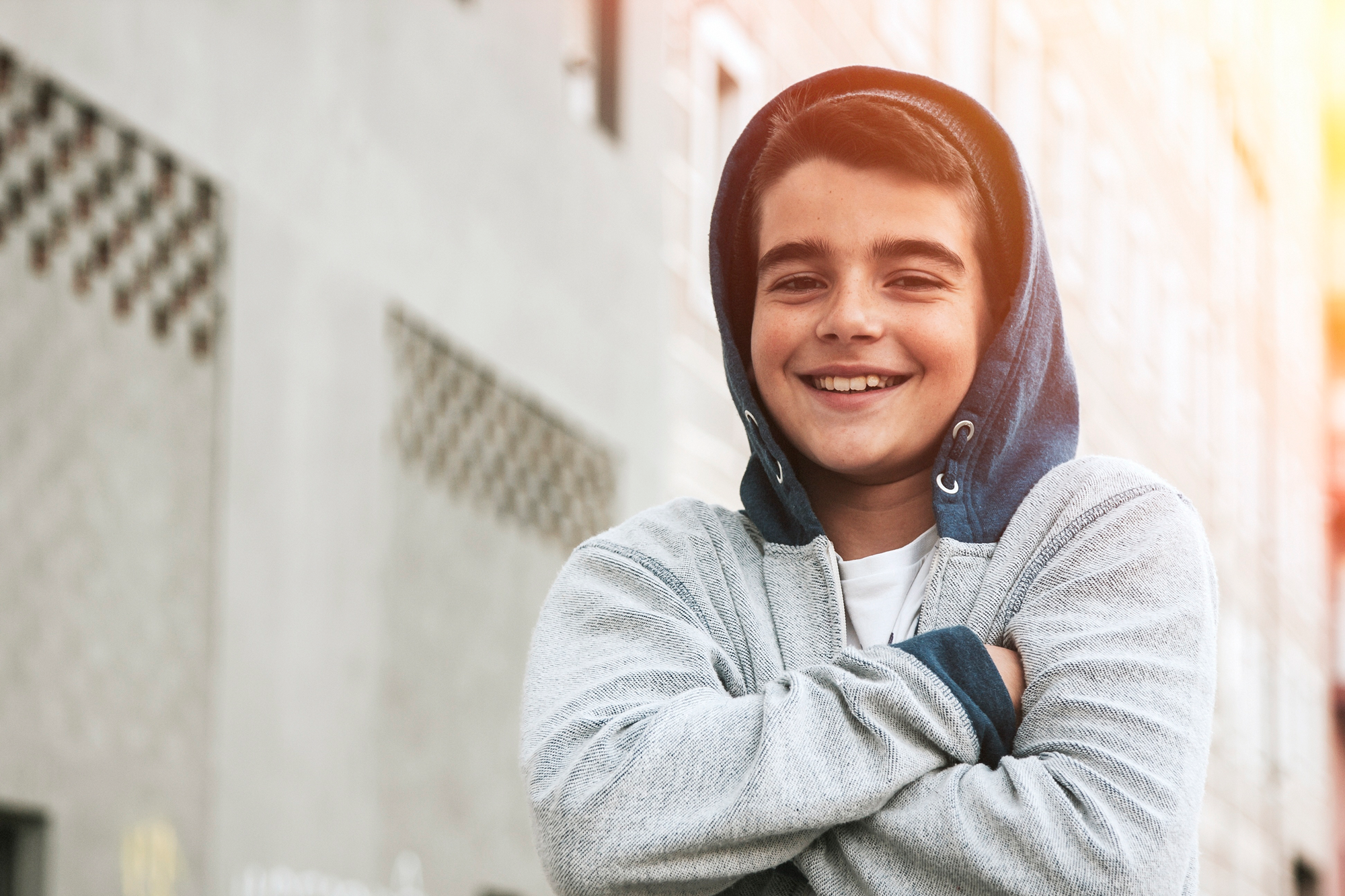 Jongen met armen over elkaar en hoodie kijkt lachend in de camera