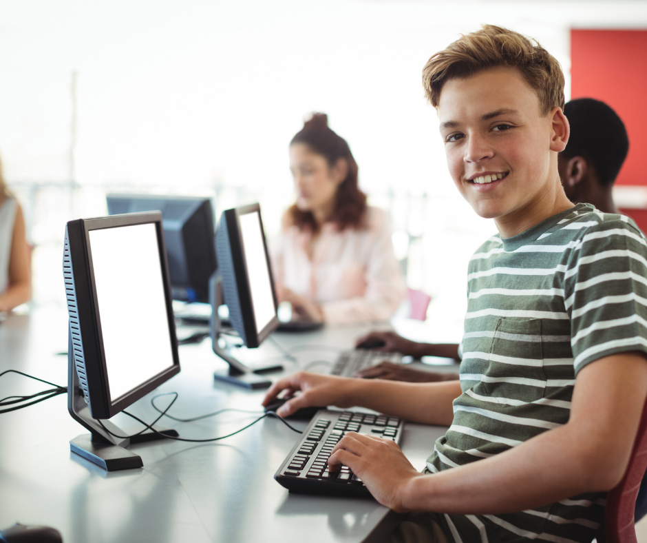 jongen in de klas kijkt glimlachend op van het beeldscherm waar hij voor zit