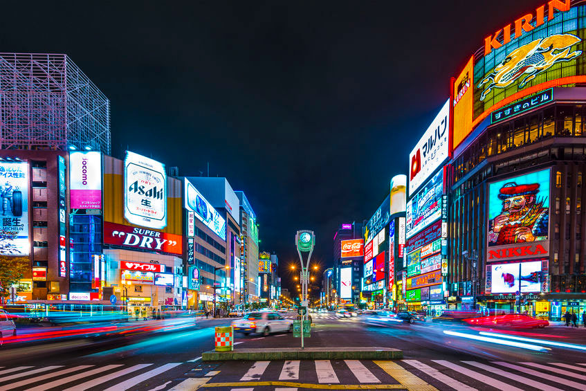 Tokio by night: kruispunt van wegen met oversteekplaatsen en gebouwen met veel kleurrijke neonreclames en afbeeldingen.