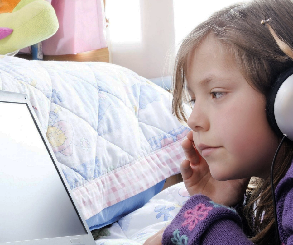 meisje met koptelefoon leest op laptop, liggend op bed