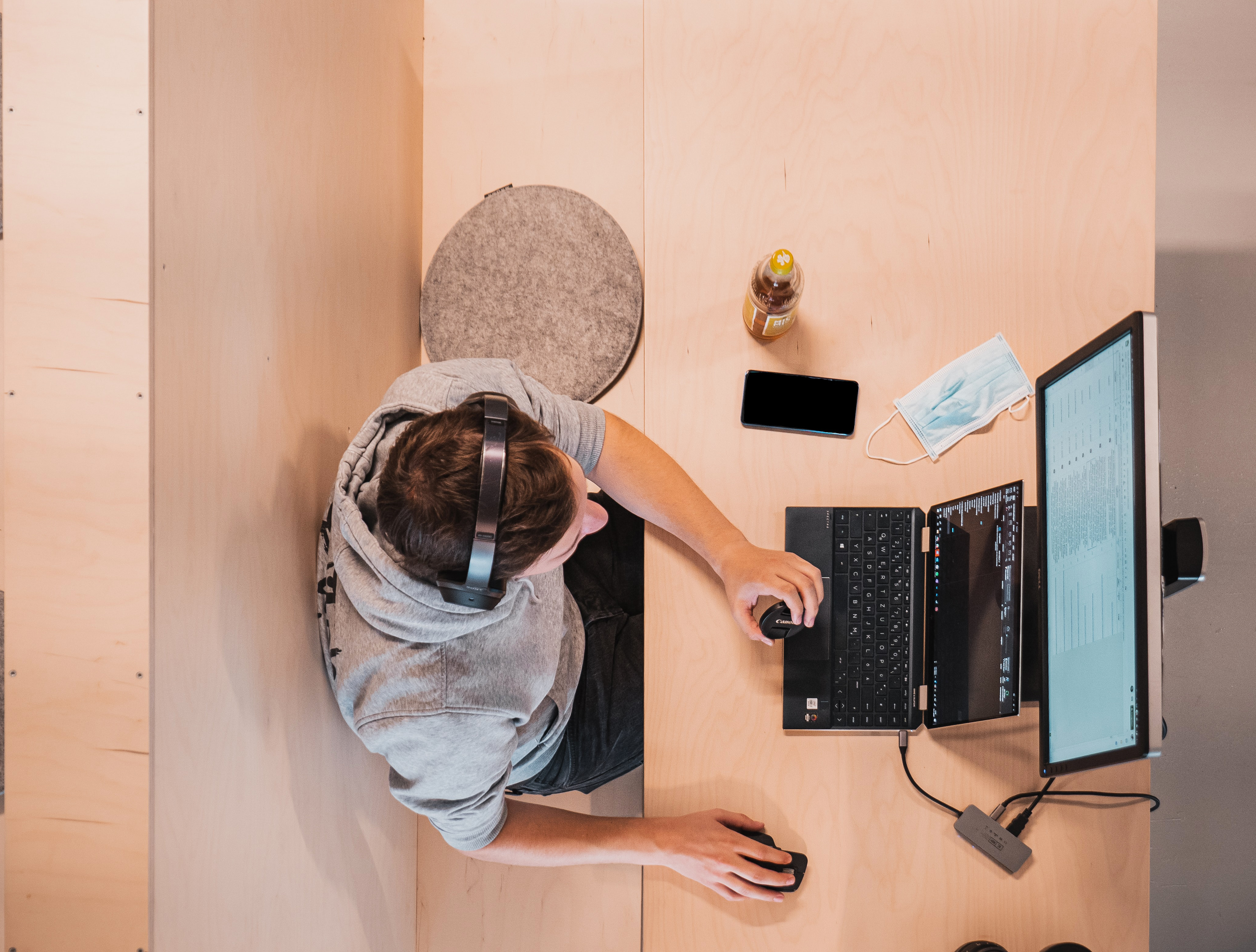 Bovenaanzicht: jongen met koptelefoon werkt met laptop. Mondkapje ligt ernaast.