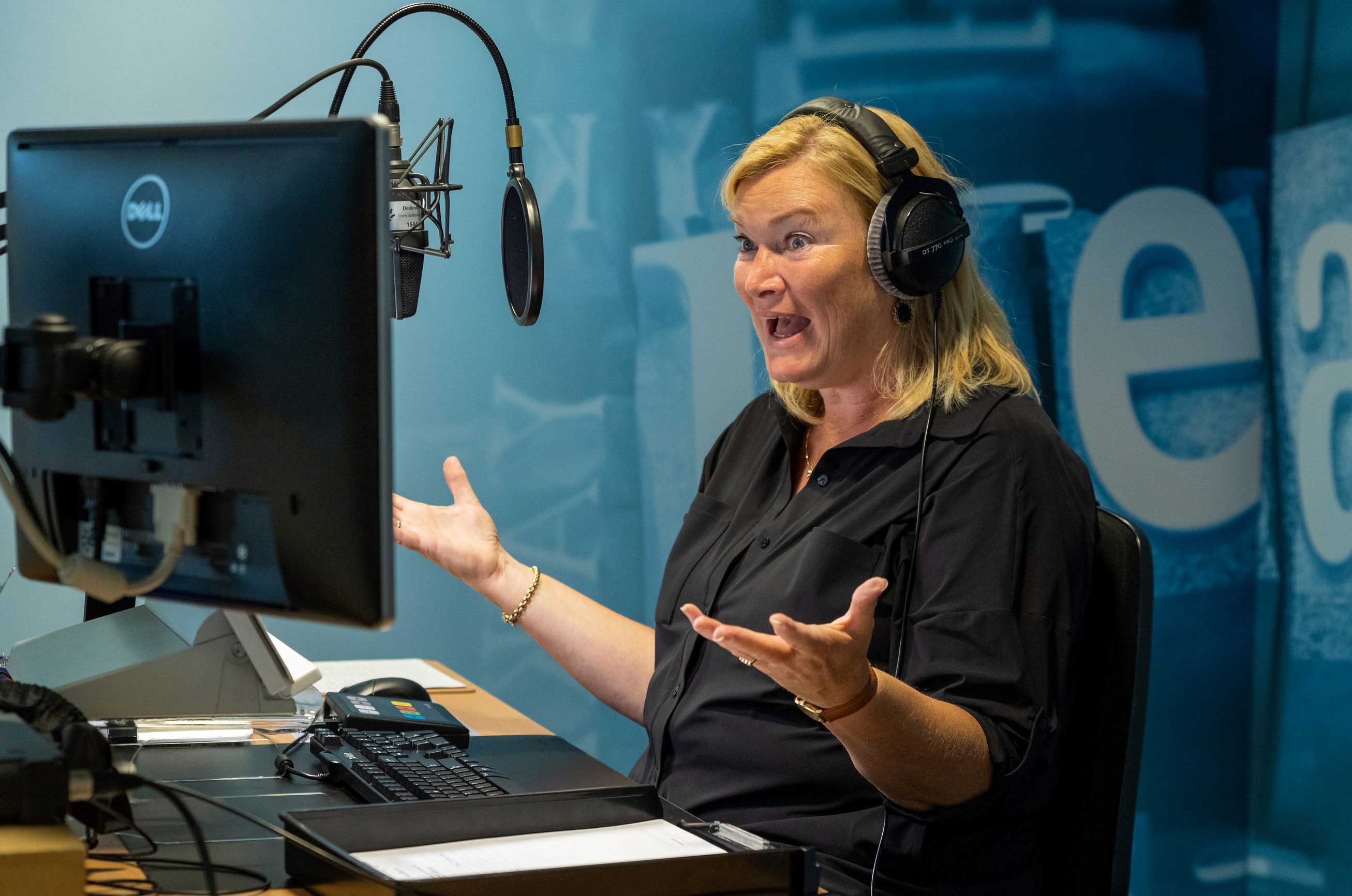 Een voorlezer spreekt met veel expressie en bewegende handen iets voor in een opnamestudio