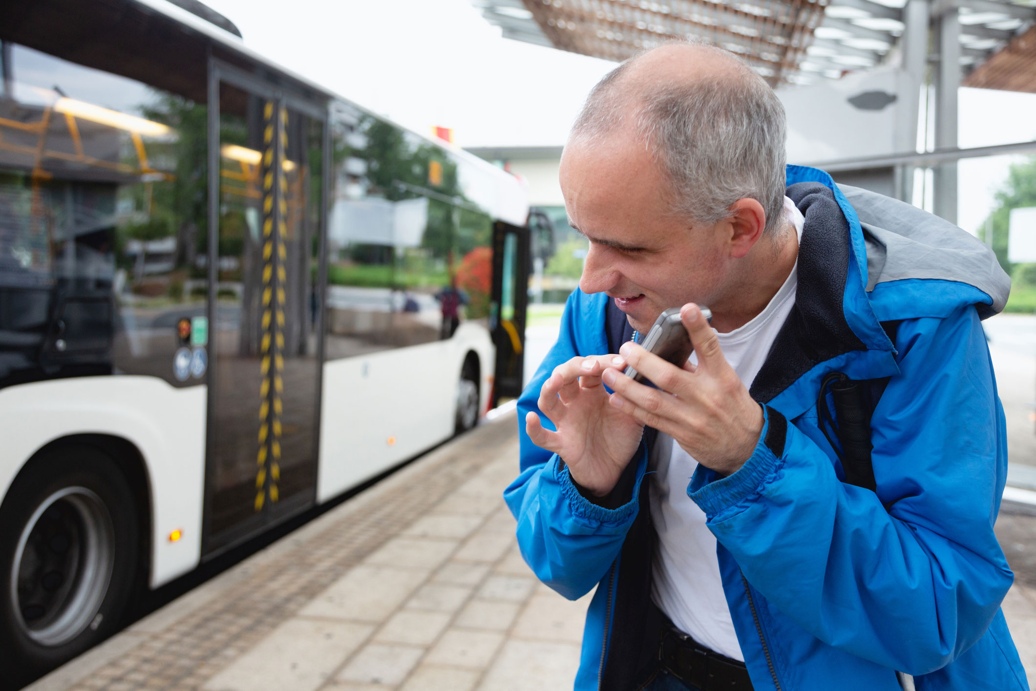 Een man staat bij de bushalte en luistert naar zijn smartphone.
