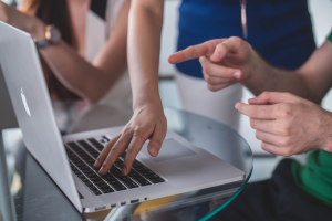 Twee paar handen bij een laptop. Een hand wijst op beeldscherm