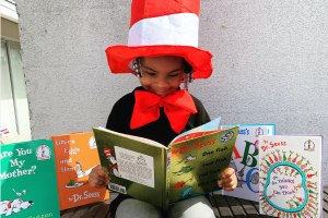 meisje met hoge gestreepte roodwitte hoed leest in een groot boek