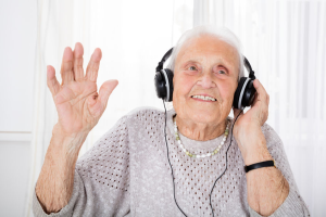 oudere vrouw geniet lachend. Met een hand houdt ze koptelefoon op haar oor vast en houdt andere hand omhoog