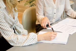 detail van twee dames die een overeenkomst tekenen aan tafel