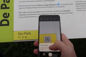Een informatiebord bij Park Lingezegen met een brailleplaatje en een QR-code die met een smartphone wordt gescand.