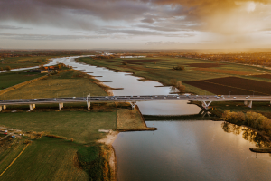 Nederlands landschapsfoto van een polder; rivier met daarover een brug waarover auto's rijden