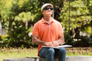een man met donkere bril zit op een bank in het park en leest een brailleboek.