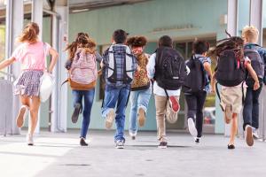 Schoolkinderen op de rug gezien, met rugzakken op, rennen weg.