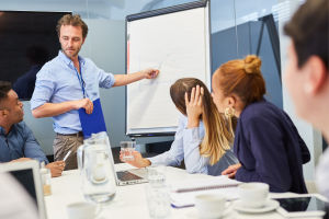 afbeelding van een man die iets uitlegt aan groep mensen, daarbij wijzend op een whiteboard