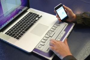 Iemand bedient zijn laptop met brailleleesregel en heeft een smartphone in de andere hand