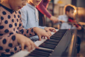 Kind speelt op keyboard. Op de achtergrond meer kinderen met muziekinstrumenten.