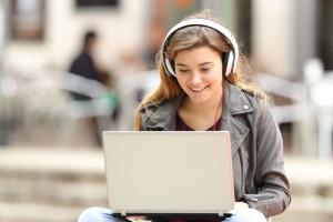 Meisje met koptelefoon kijkt op laptop