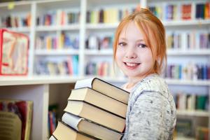 Meisje met rood haar houdt stapel boeken vast. Ze staat in de klas.