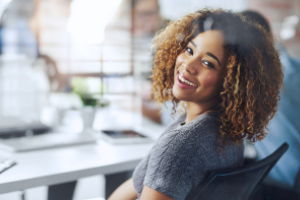 dame gezeten aan bureau kijkt lachend over haar schouder naar achteren