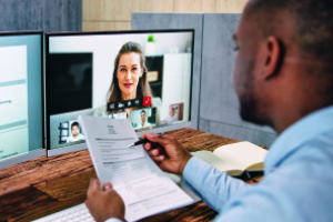 videobewerking door iemand (deels in beeld) die een document met tekst vasthoudt en op achtergrond twee beeldschermen