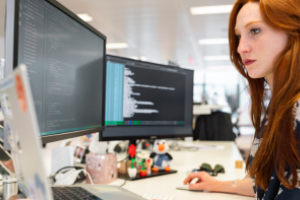 jonge vrouw werkend aan bureau met computer en beeldschermen