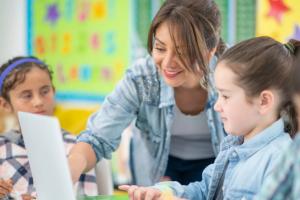 Een leerling achter een laptop met een lerares