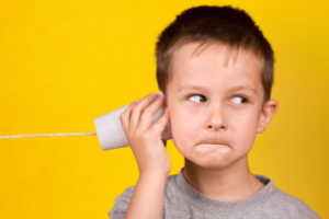 jongen kijkt naar rechts terwijl hij een blikje met daaraan een touw aan zijn oor houdt