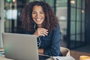 Een vrouwelijke it-medewerker zit achter een laptop en heeft oortjes in.
