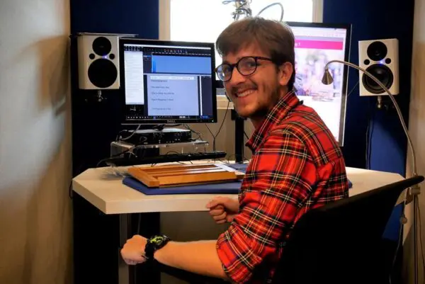 Een voorlezer zit in een studiocabine met beeldscherm en microfoon