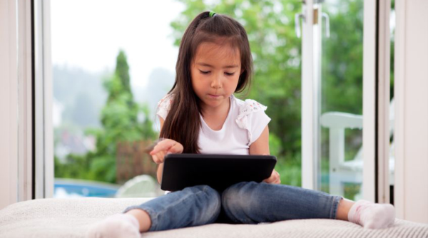 meisje zit op een kussen met tablet op schoot