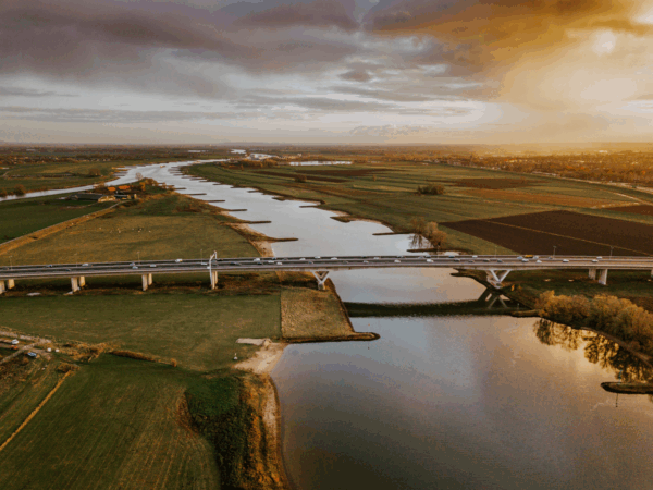 Nederlands landschapsfoto van een polder; rivier met daarover een brug waarover auto's rijden