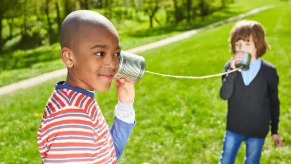 Twee kinderen hebben ieder een blikje in de hand; de een bij het oor en de ander spreekt erin. Tussen de twee blikken zit een touwtje.