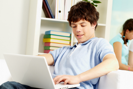 Jongen werkt met een laptop terwijl hij op de bank zit. 