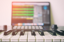 Keyboard op de voorgrond. Op de achtergrond een laptop met een muziekprogramma