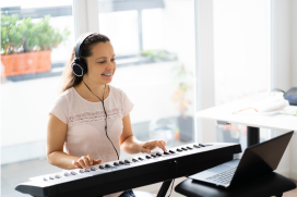 Kind bespeelt keyboard terwijl het met een koptelefoon luistert naar de muziek via de laptop.