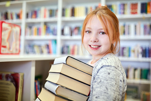 Meisje met rood haar houdt stapel boeken vast. Ze staat in de klas.